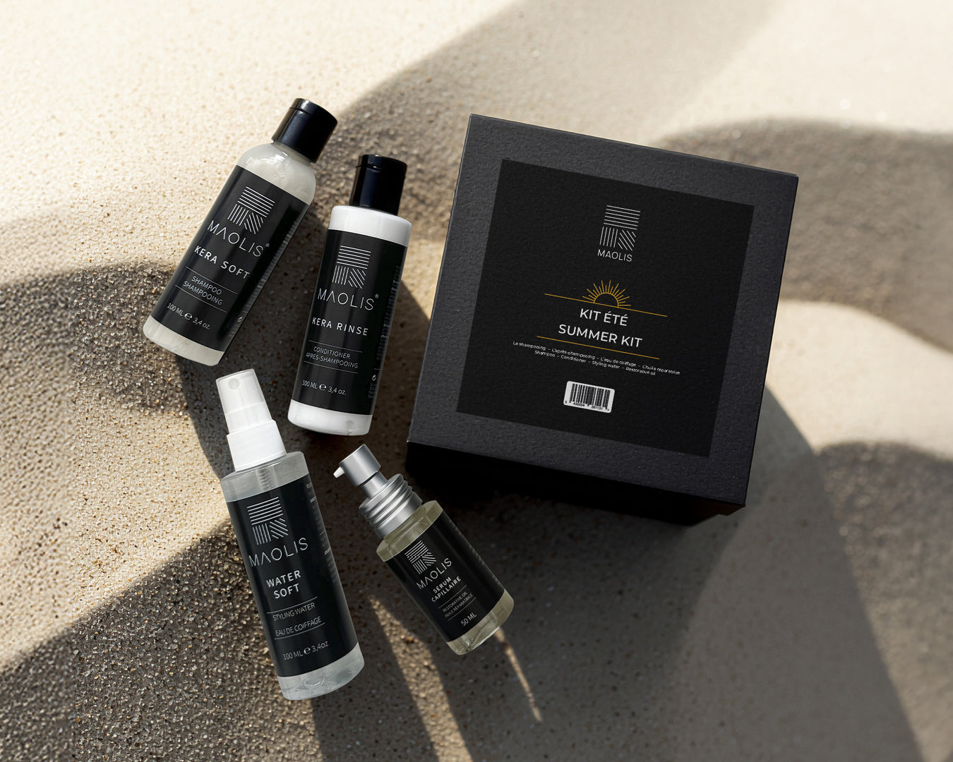 Coffret carré noir Kit été MAOLIS, avec ces quatre produits posés sur le sable. Ambiance été